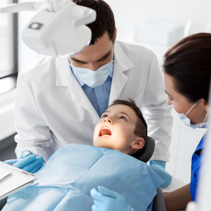 Young Male Getting Teeth Cleaned by 2 Dentists